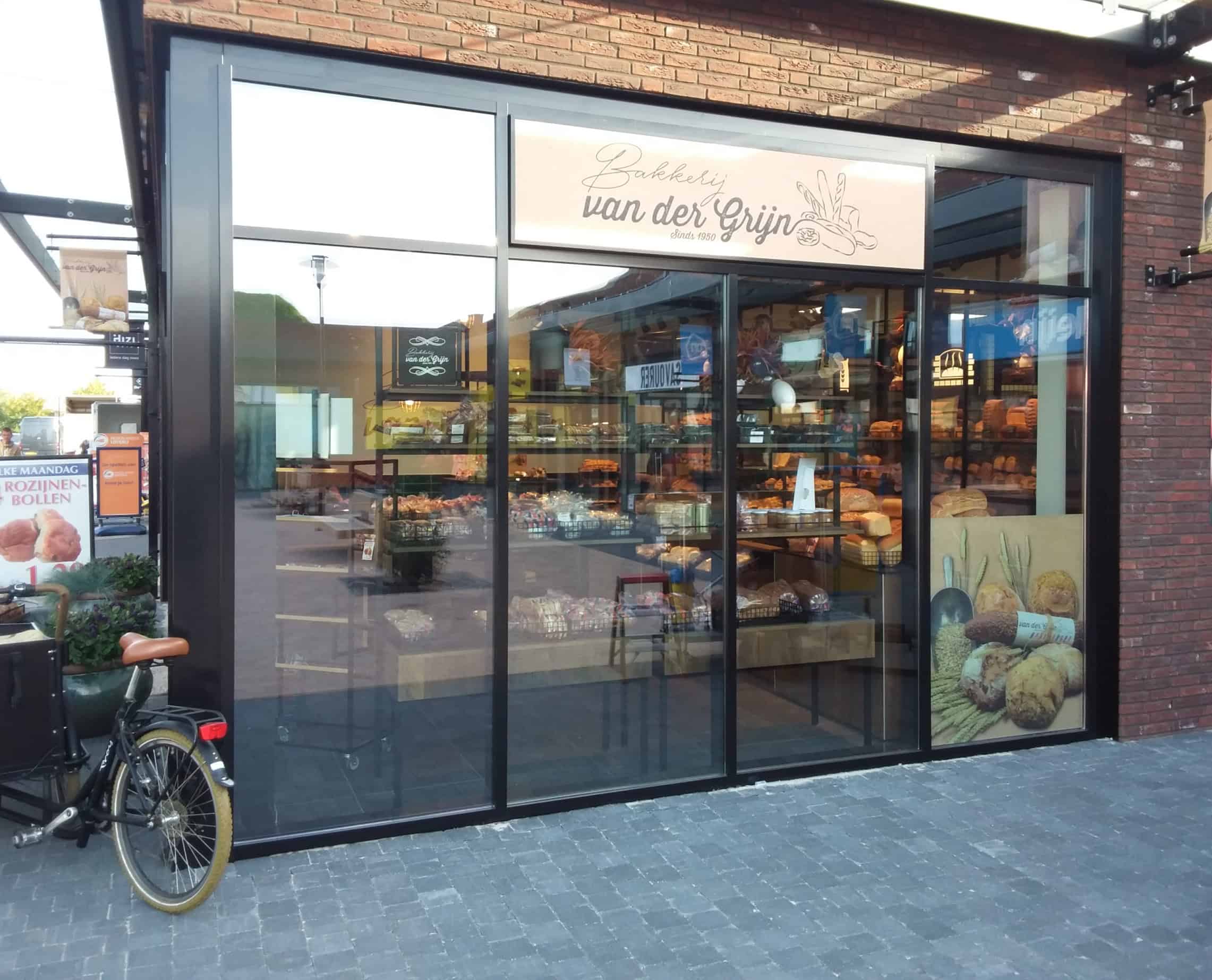 Een moderne bakkerij met grote glazen ramen, een display vol vers brood en een fiets geparkeerd voor de ingang. Hier hebben we Sentinel SX 50, een licht spiegelende zonwerende folie, aangebracht om vooral de etenswaren te beschermen tegen zonlicht.