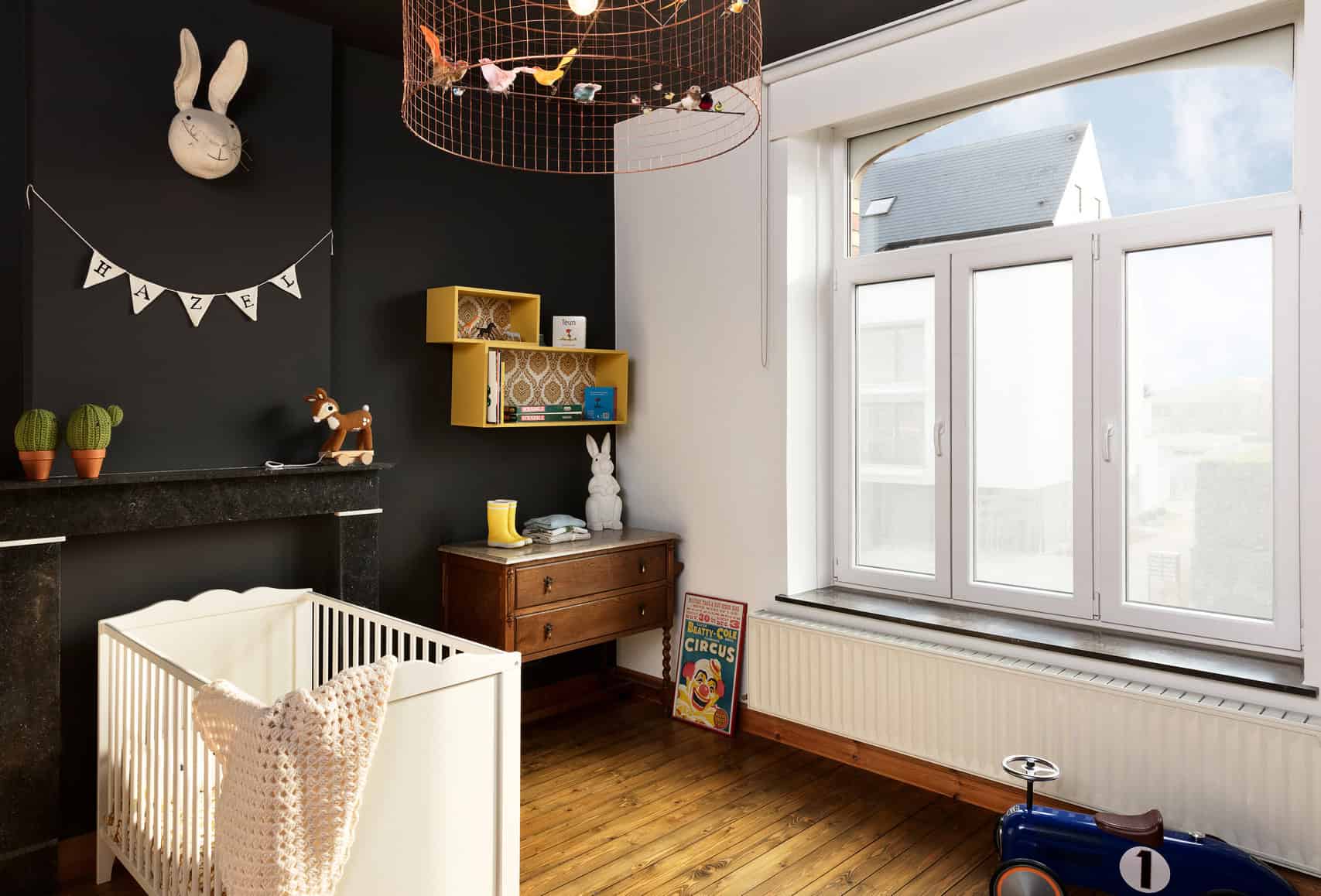 3T5A9744-3 Een interieurfoto van drie ramen in een huis, elk voorzien van decoratief glas in de bovenste delen, met een kleurrijk patroon van gele en oranje tinten. Het onderste gedeelte van de ramen heeft matte folie, die privacy biedt terwijl het uitzicht naar buiten behouden blijft. De ramen zijn typisch voor een oud huis, met een klassieke uitstraling door de combinatie van het glas-in-lood boven en het moderne matte folie eronder. In de achtergrond zijn andere huizen zichtbaar.